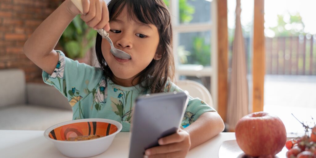 Criança a comer cereais e a olhar para o telemóvel